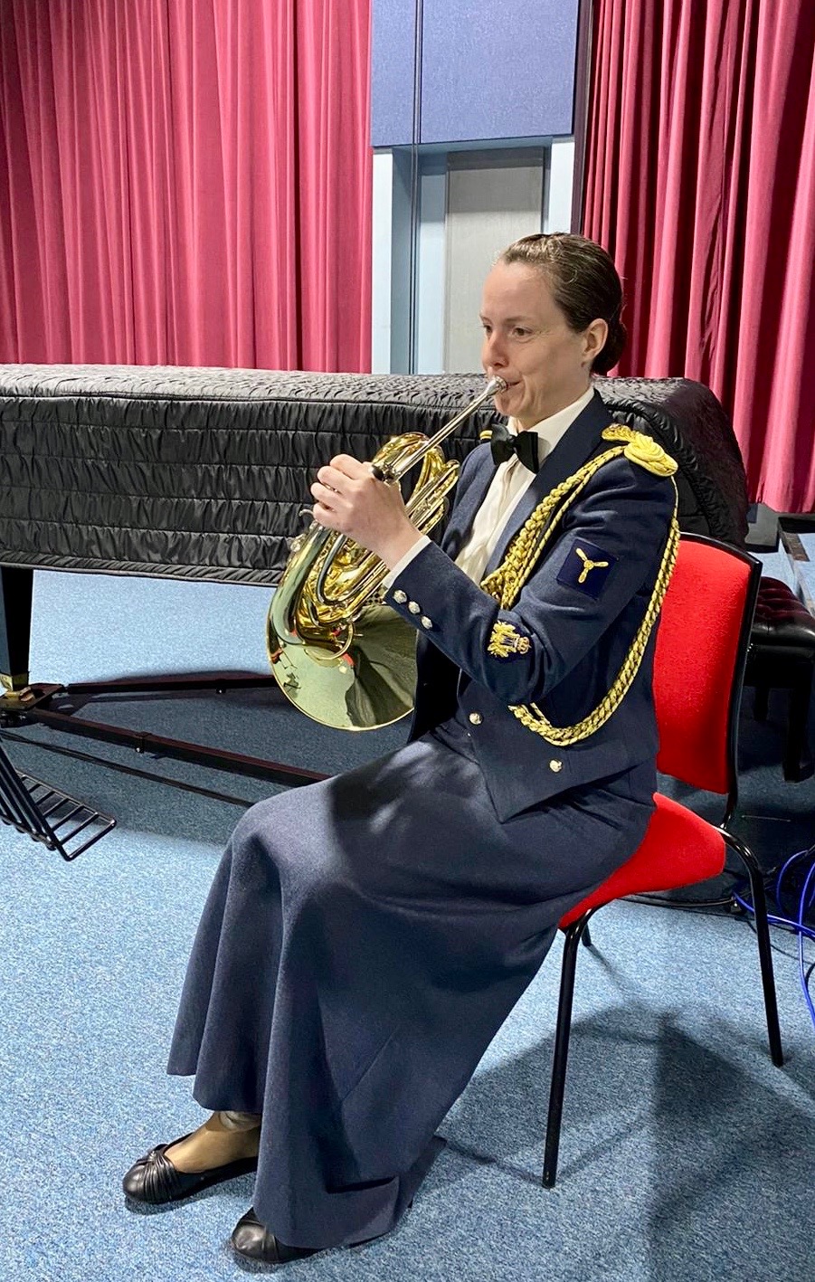 RAF Musician sat on a chair while playing a French Horn.